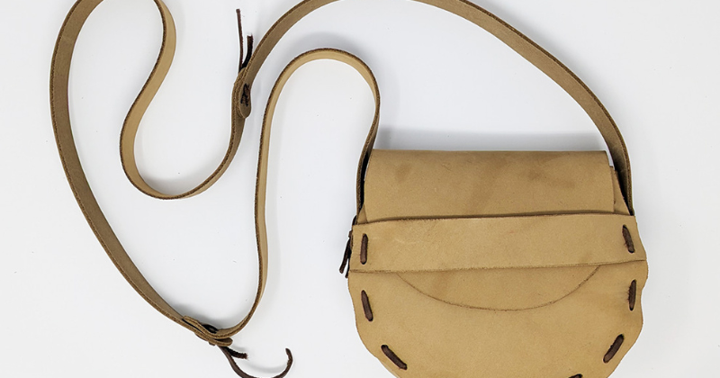 A tan laced leather shoulder bag with a long strap on a white background.
